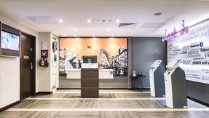 A hotel reception area with a digital check-in kiosk, a reception desk, and a large wall with motivational posters. - Premier Inn Wokingham Town Centre (Wokingham)