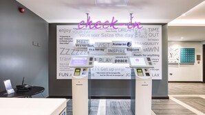 A hotel reception area with two self-service kiosks, a reception desk, and motivational posters on the wall. - Premier Inn Wokingham Town Centre (Wokingham)