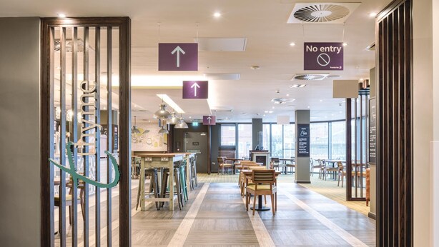 A modern hotel lobby with directional signs, a reception desk, and seating areas. - Premier Inn Wokingham Town Centre (Wokingham)