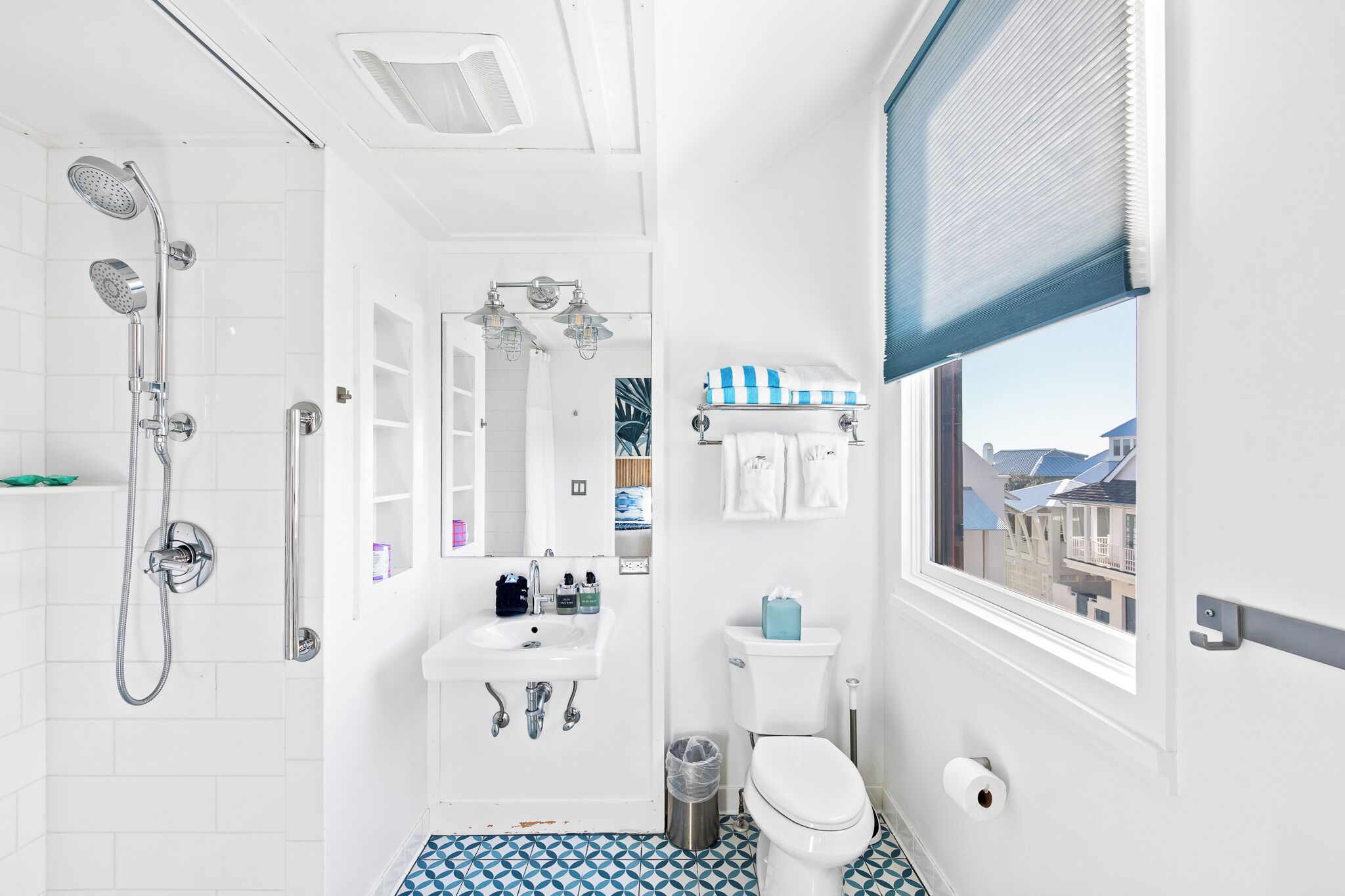 A modern bathroom with a shower, sink, toilet, and a window with a view of buildings.