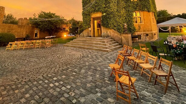 A building with ivy-covered walls, a cobblestone courtyard, and wooden chairs arranged for an event. - Majestic 17th-century castle in stunning Somerset countryside. Pet friendly. (Clevedon)