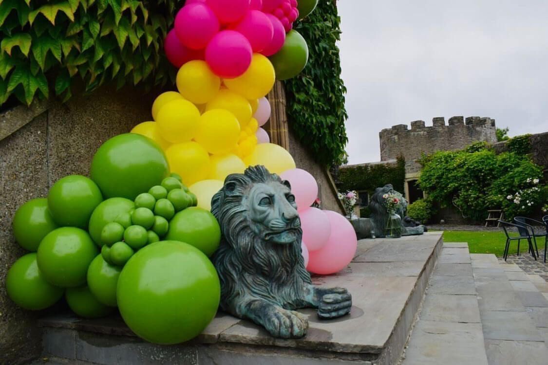 A stone lion statue in a courtyard with colorful balloons arranged in a pyramid shape.
