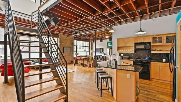 Un loft espacioso con escalera de madera, cocina con armarios de madera y un ventanal que proporciona luz natural.
