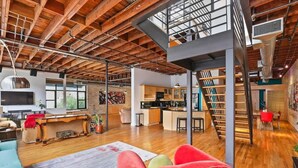 Un loft amplio con vigas de madera a la vista, un nivel entre piso, una zona de cocina y un espacio de estar con un gran ventanal.
