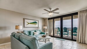 Ein Wohnzimmer mit einer Couch, einem runden Couchtisch, einem Deckenventilator und einem großen Fenster mit Blick auf den Strand.