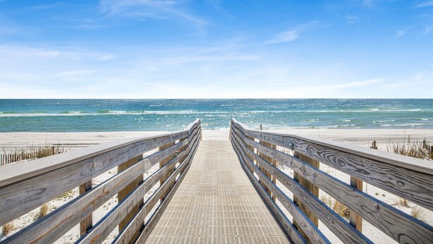Ein hölzerner Steg führt zu einem Strand unter blauem Himmel.