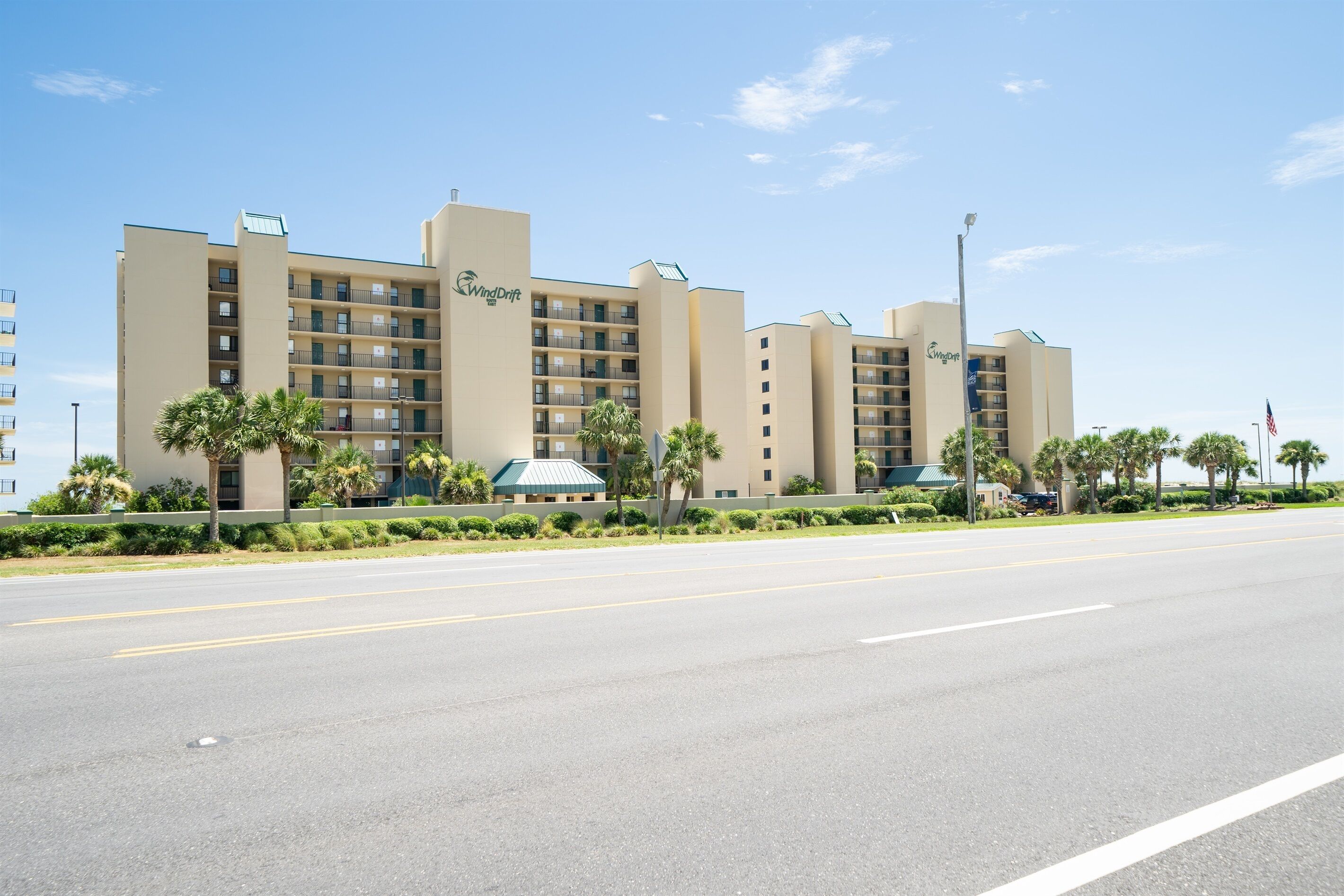 A multi-story hotel with a flat roof, balconies, and a landscaped front yard with palm trees.