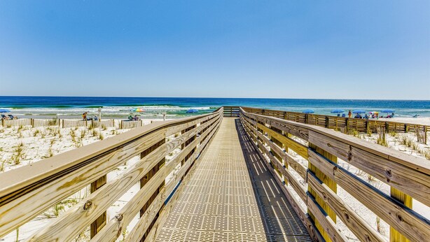 A wooden boardwalk leading to a beach with umbrellas and people. - Orange Beach Gulf-Front 3BR • Sleeps 10 • Bunk Room • Games • Oversized Balcony (Orange Beach)