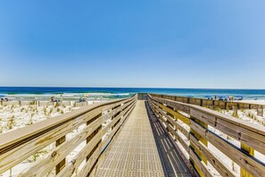 A wooden boardwalk leading to a beach with umbrellas and people. - Orange Beach Gulf-Front 3BR • Sleeps 10 • Bunk Room • Games • Oversized Balcony (Orange Beach)