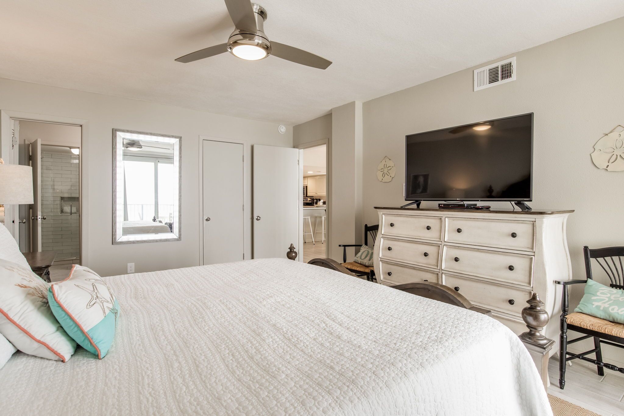 A bedroom with a large bed, a ceiling fan, a TV, a dresser, and a chair.