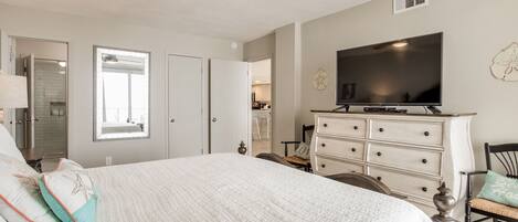 A bedroom with a large bed, a ceiling fan, a TV, a dresser, and a chair.