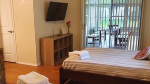 Une chambre d’hôtel avec un lit, une télévision, une table de chevet en bois et une vue sur la terrasse extérieure.