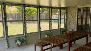Un patio couvert avec une table et des bancs en bois, de grandes fenêtres et des plantes en pot.