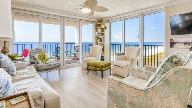 Un salon spacieux avec un balcon donnant sur la mer, équipé d’un ventilateur de plafond, d’une bibliothèque et de sièges confortables.