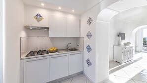 A modern kitchen with white cabinets, a gas stove, and a sink. There are decorative tiles on the walls and a view of the outside through an archway. - Villa dei Lecci Blu - luxury villa with terrace on the sea (Forio)