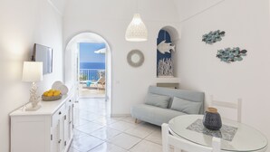 A modern, well-lit living room with a sofa, a glass table, and a view of the sea through an open archway. - Villa dei Lecci Blu - luxury villa with terrace on the sea (Forio)