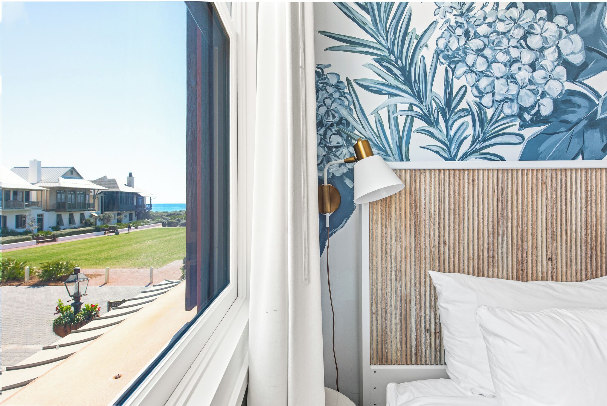 Habitación de hotel con vistas a la calle, una cama con ropa blanca, una lámpara de pared y un panel de pared de madera.
