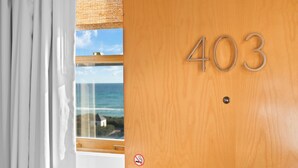 Una puerta de madera con el número 403, una ventana con vista al mar y un cartel de prohibido fumar.