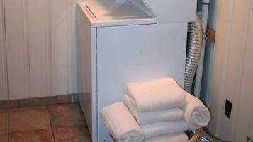 A compact laundry room with a stacked washer and dryer, a basket of folded towels, and a visible water pipe.