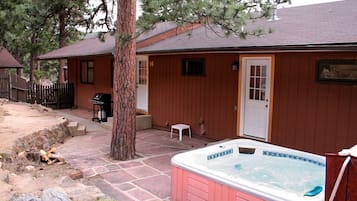 A wooden cabin with a hot tub, stone patio, and a barbecue area.