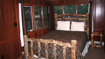 A wooden-framed bed with a patterned bedspread in a room with wooden walls and large windows.