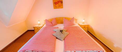 A single bed with a checkered bedspread, two pillows, a nightstand with a lamp, and a painting on the wall.