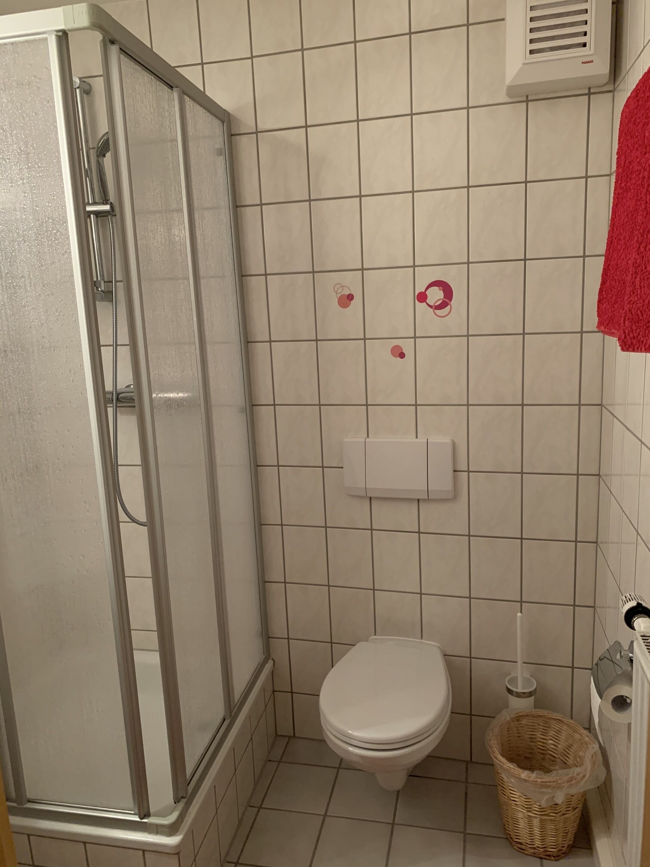 A bathroom with a glass-enclosed shower, a toilet, and a trash bin.