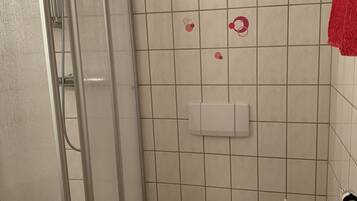 A bathroom with a glass-enclosed shower, a toilet, and a trash bin.