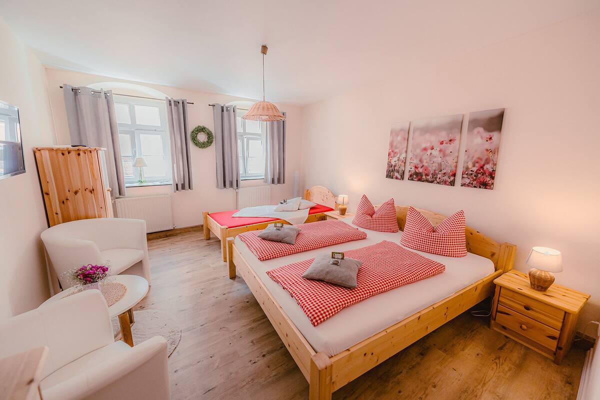 A bedroom with two beds, a wooden wardrobe, a small table with flowers, and a wall with floral artwork.