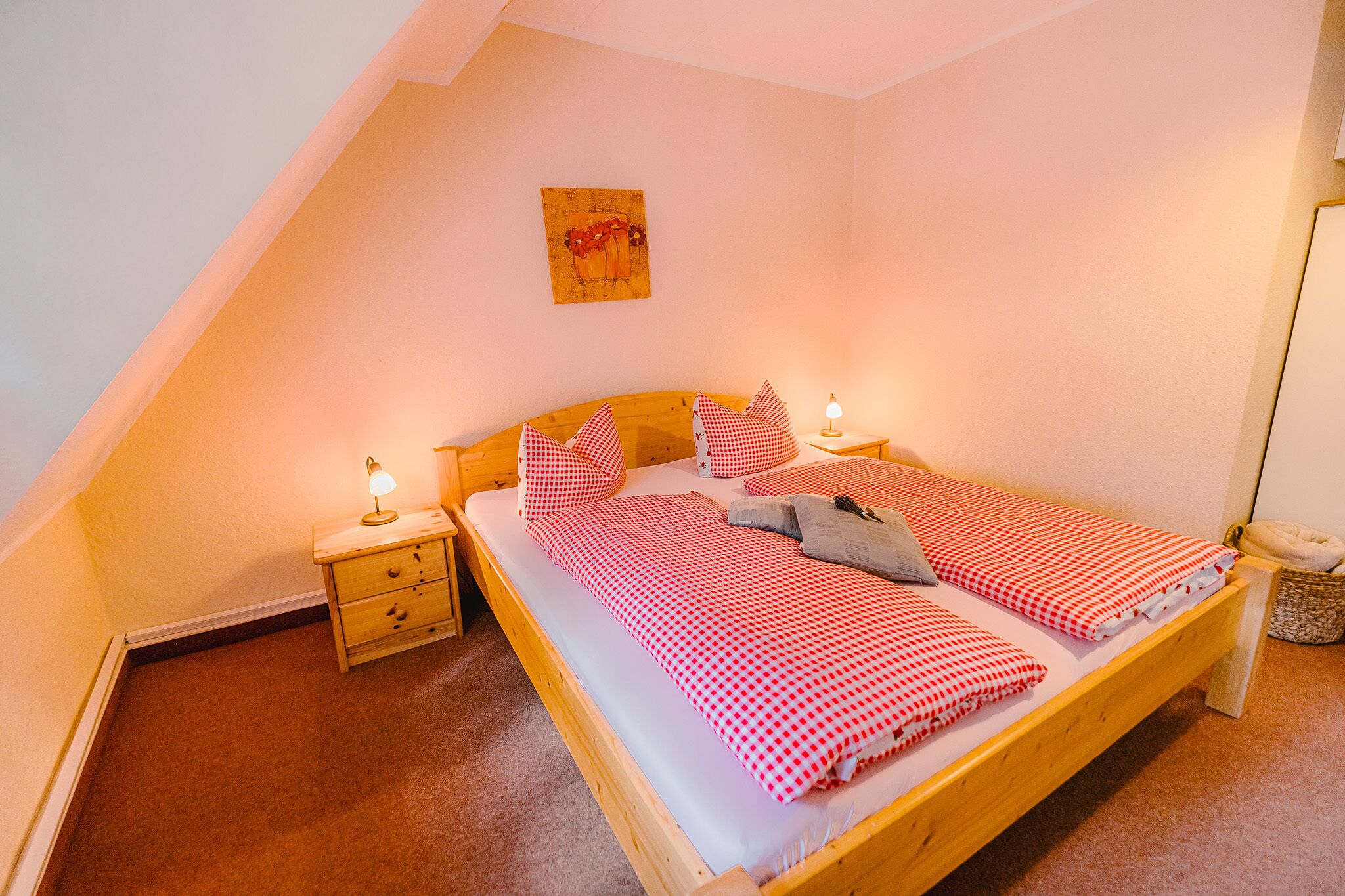 A single bedroom with a wooden bed, two bedside tables, a nightstand, a lamp, a small rug, and a wall-mounted artwork.