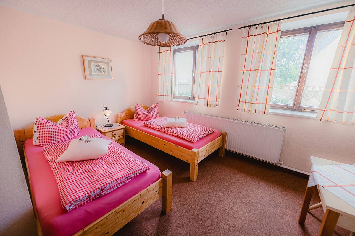 A bedroom with two wooden beds, a bedside table, a lamp, and a window with curtains.