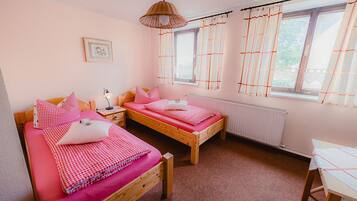 Un dormitorio con dos camas de madera, una mesita de noche, una lámpara y una ventana con cortinas.