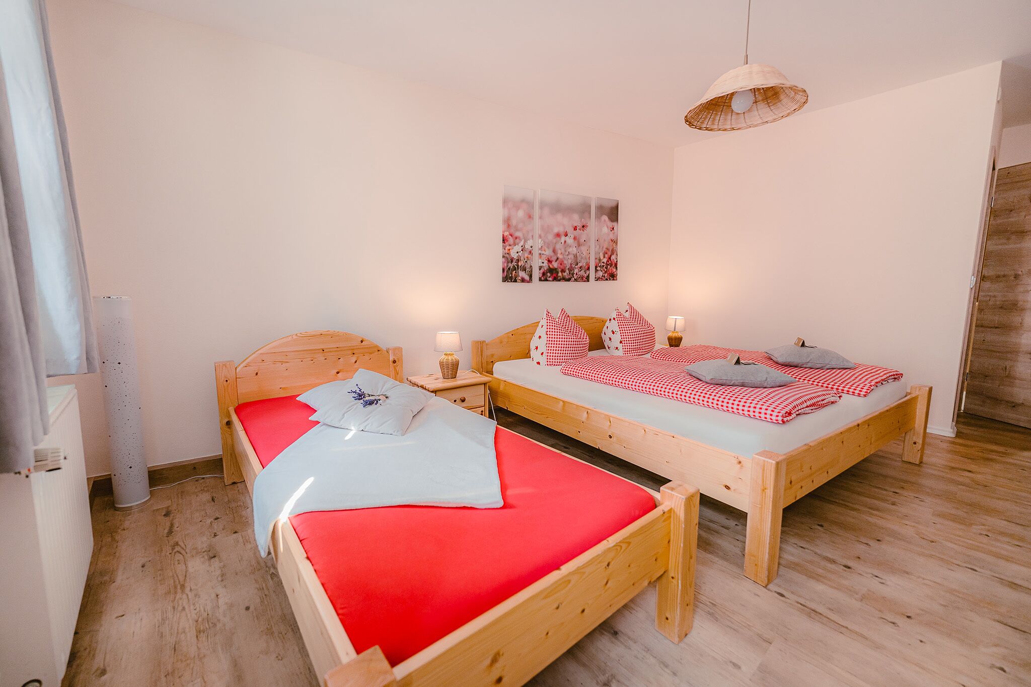 A room with two wooden beds, each with red bedding and pillows, a wooden nightstand with a lamp, and a wall-mounted picture.