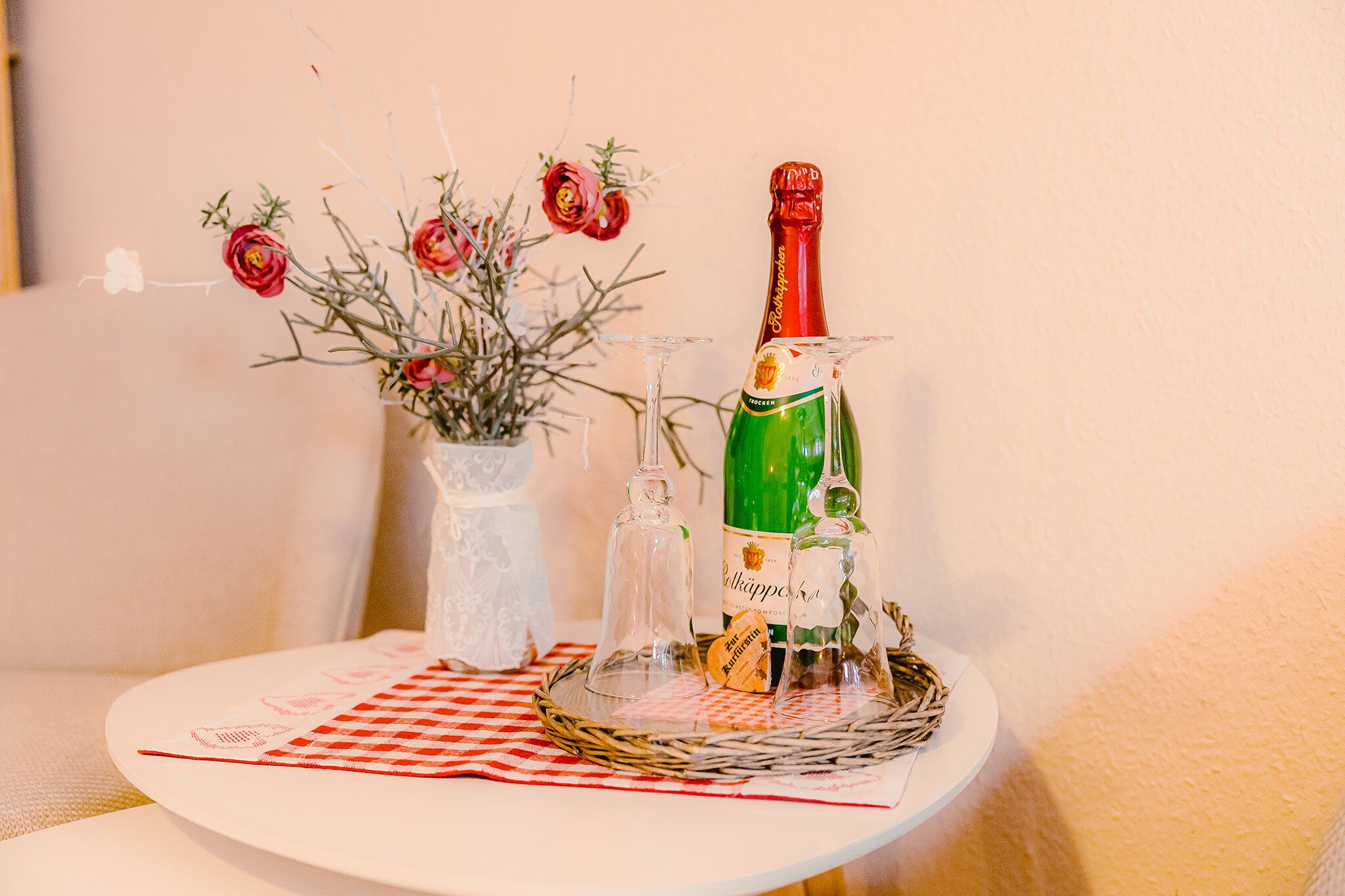 A table with a bottle of champagne, a glass, and a vase with flowers.