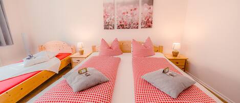 A double room with two beds, each with red and white checkered bedding and gray pillows. There are bedside tables with lamps and a wall-mounted artwork above the beds.