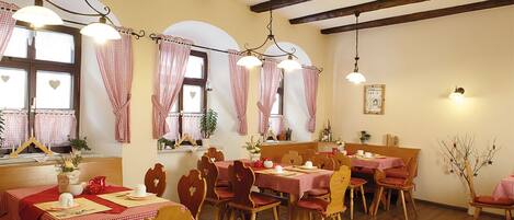 Un comedor con mesas y sillas de madera, manteles a cuadros blancos y rojos, y lámparas colgantes.