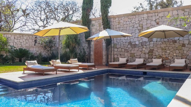A swimming pool with lounge chairs and umbrellas, surrounded by stone walls and greenery. - Gamma Morelia Vista Bella (Morelia)