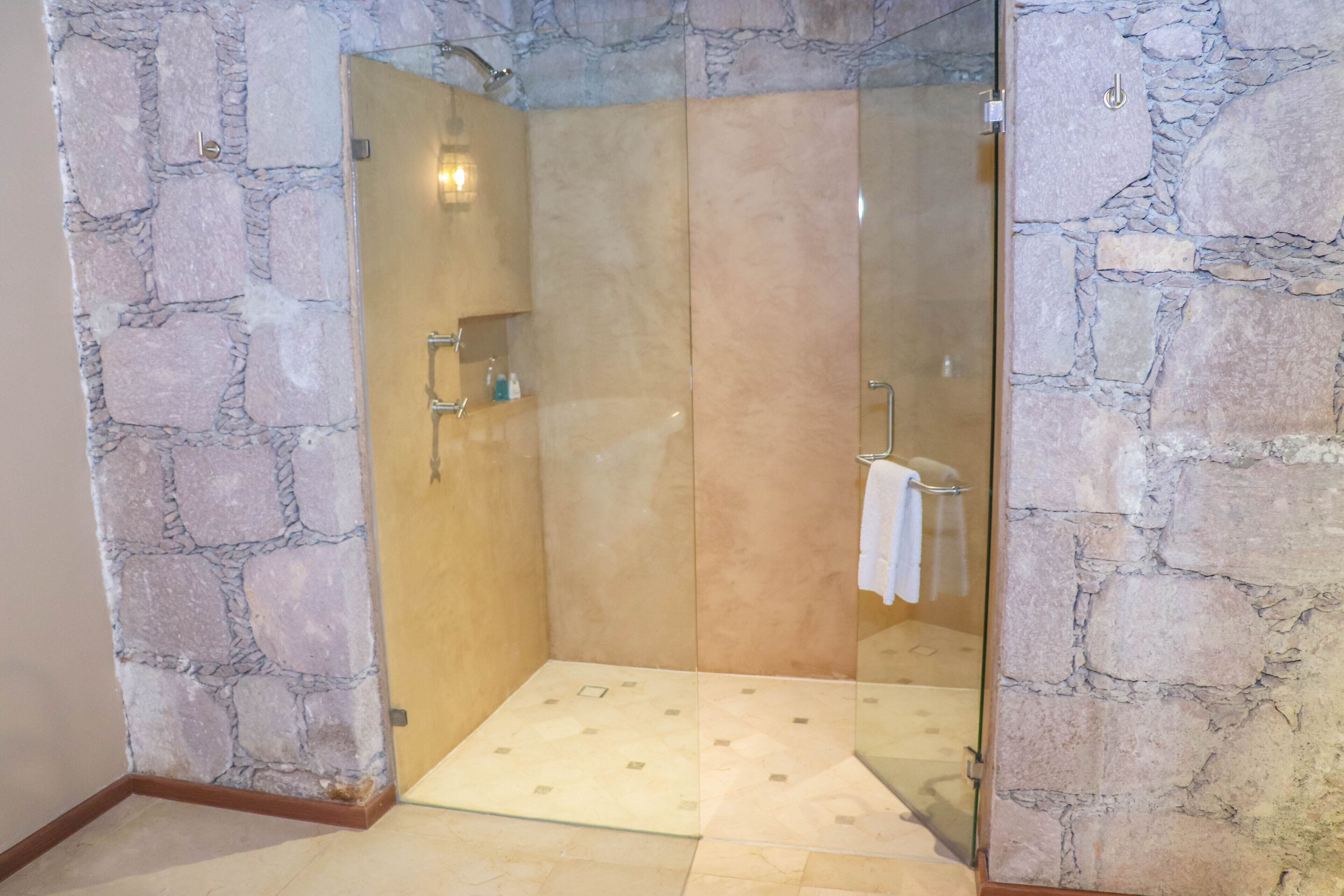 A glass-enclosed shower with stone walls and a tiled floor.