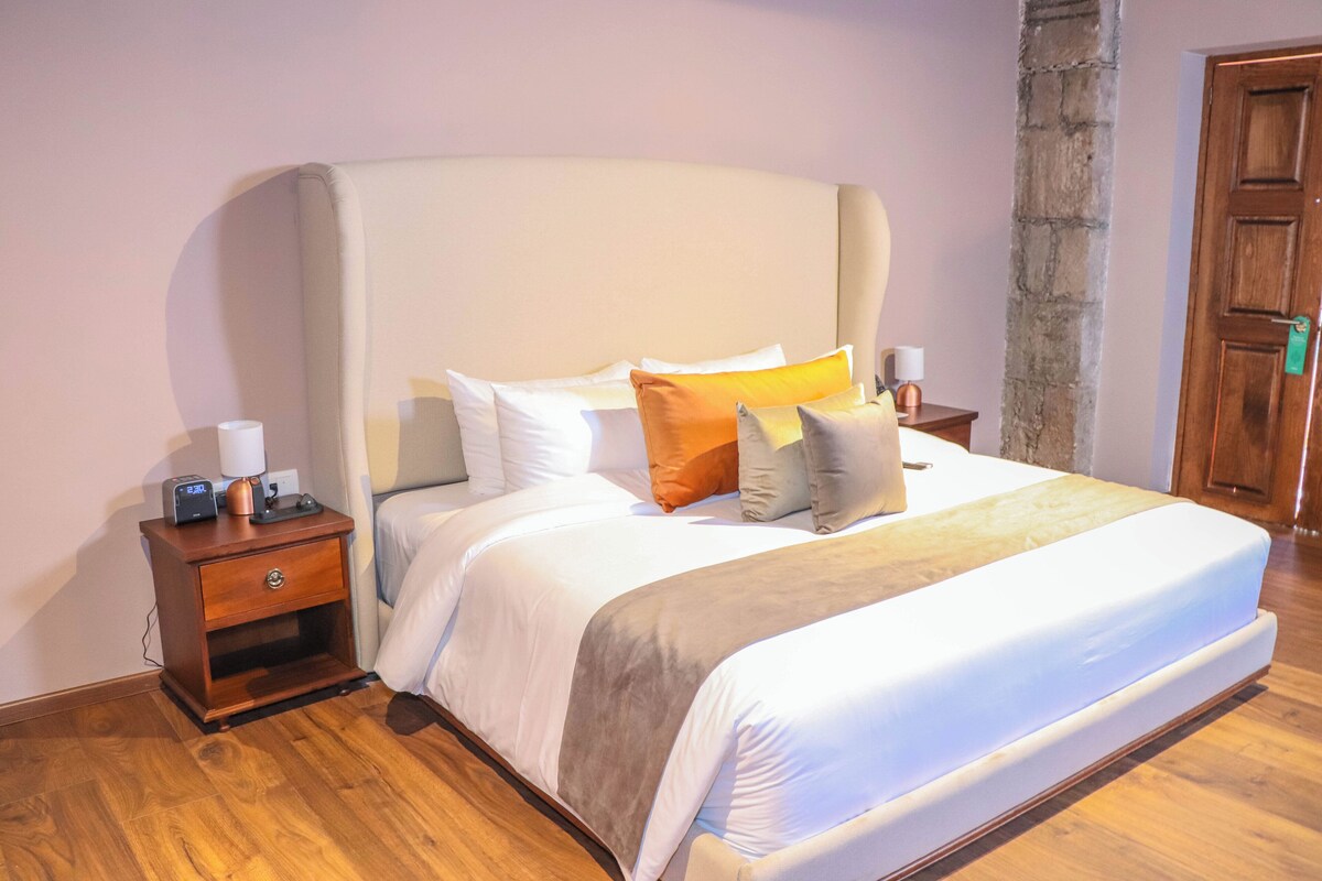 A neatly made bed with a headboard, a bedside table with a lamp, and a wooden nightstand.