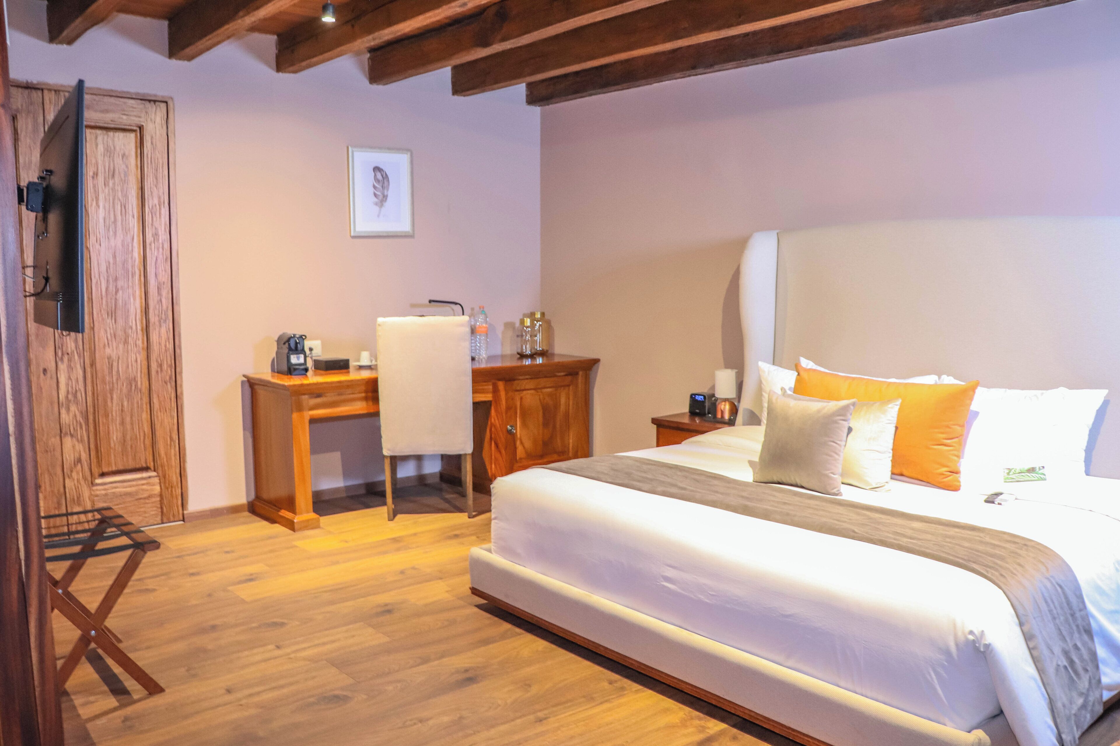 A bedroom with a large bed, wooden desk, chair, and a wooden door.