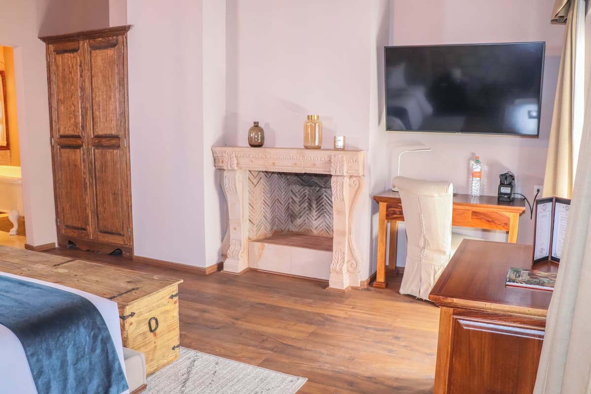 Una habitación con un armario de madera, una chimenea con adornos, un televisor y un escritorio con una silla.