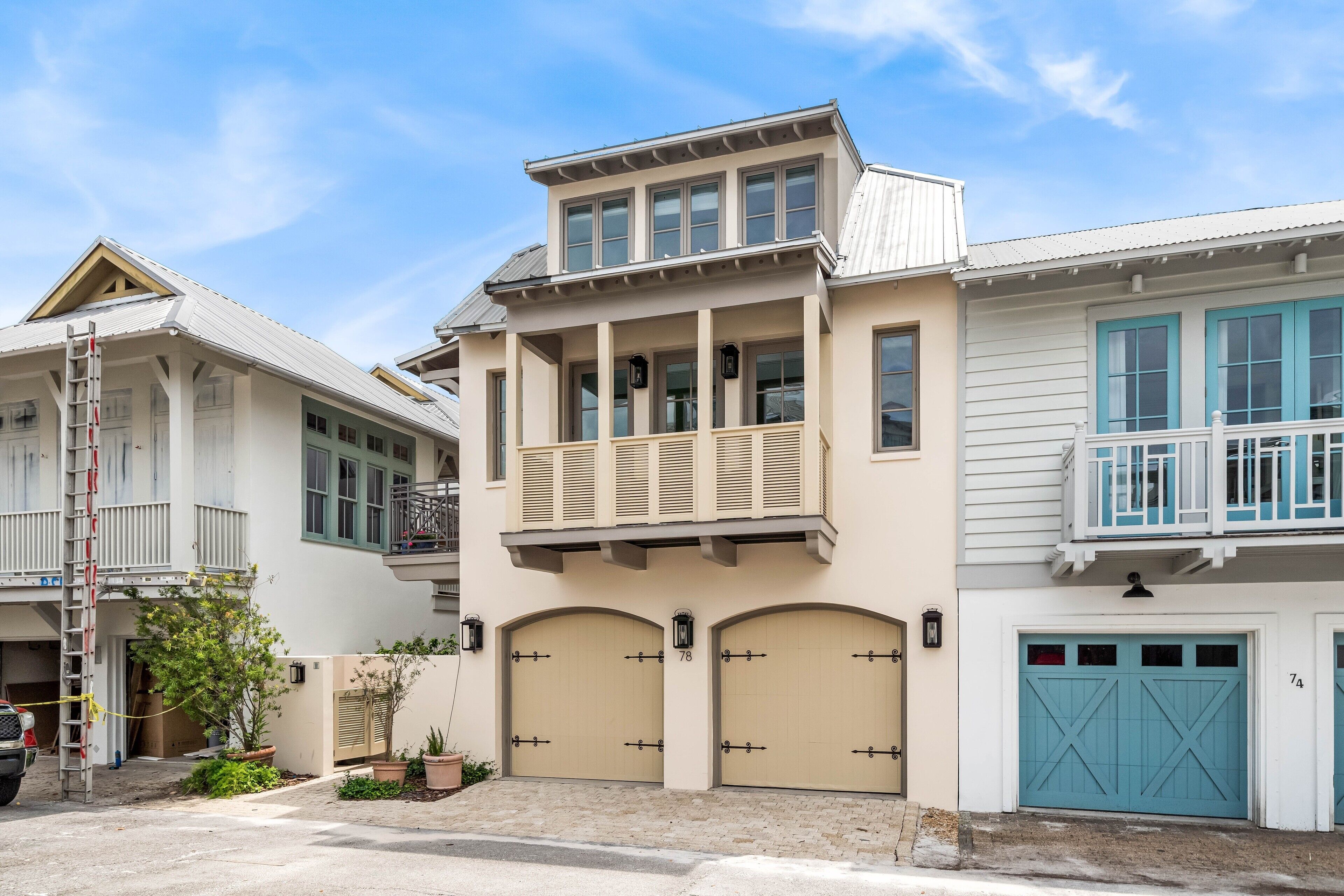 A two-story house with a balcony, beige garage doors, and a blue garage door.