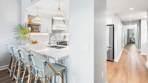 A modern kitchen with white cabinetry, a marble countertop, and a central island with bar stools.