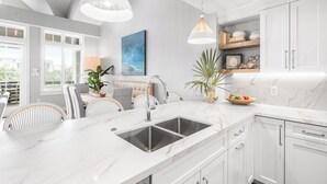 A modern kitchen with white cabinetry, a marble countertop, and pendant lighting.