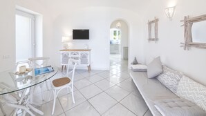 A modern living room with a glass dining table, white furniture, a sofa, and a TV mounted on the wall. - Villa dei lecci Indaco - Luxury villa on the sea with private jacuzzi (Forio)