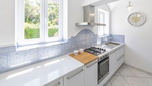 A modern kitchen with white cabinetry, a gas stove, and a large window overlooking greenery. - Villa dei lecci Indaco - Luxury villa on the sea with private jacuzzi (Forio)