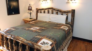 A bed with a rustic wooden headboard, a quilt with animal prints, and wall-mounted lights. - Stonehaven Home (Estes Park)