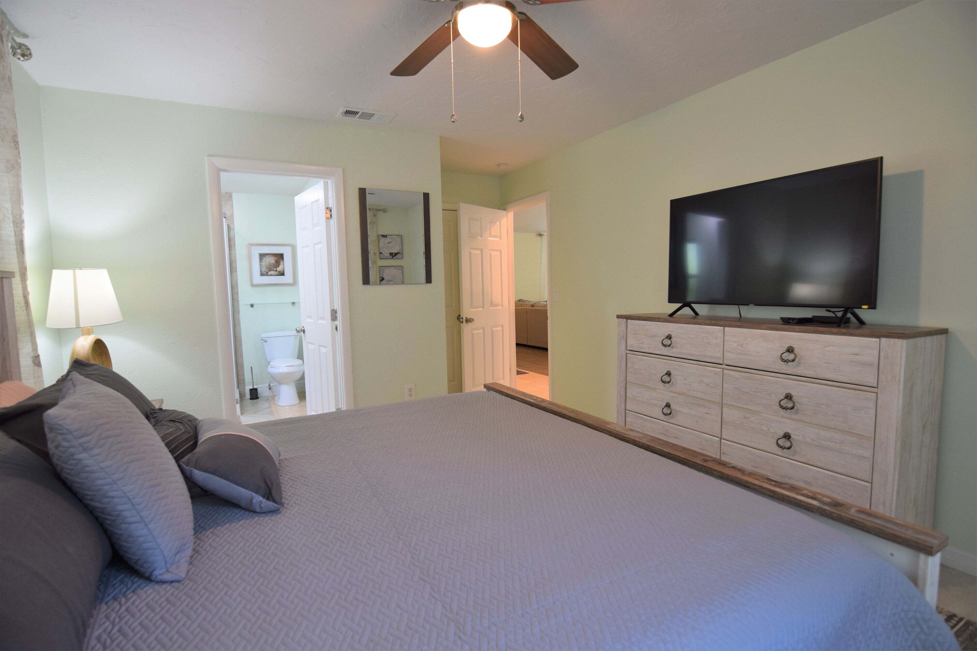 A bedroom with a bed, a dresser, a television, and a ceiling fan.
