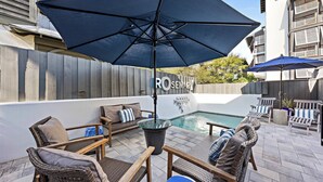 Une terrasse avec des meubles en osier, une piscine et des parasols.