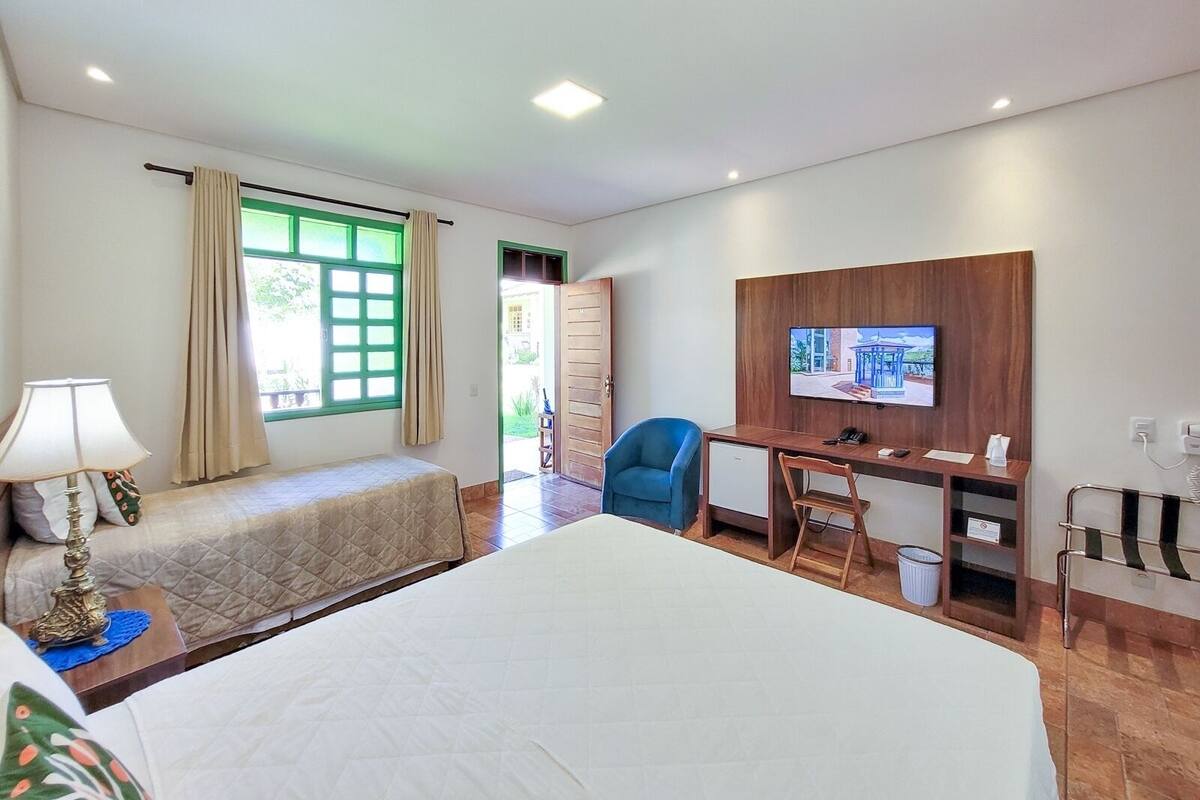 A hotel room with a bed, a desk with a chair, a TV, and a window with curtains.